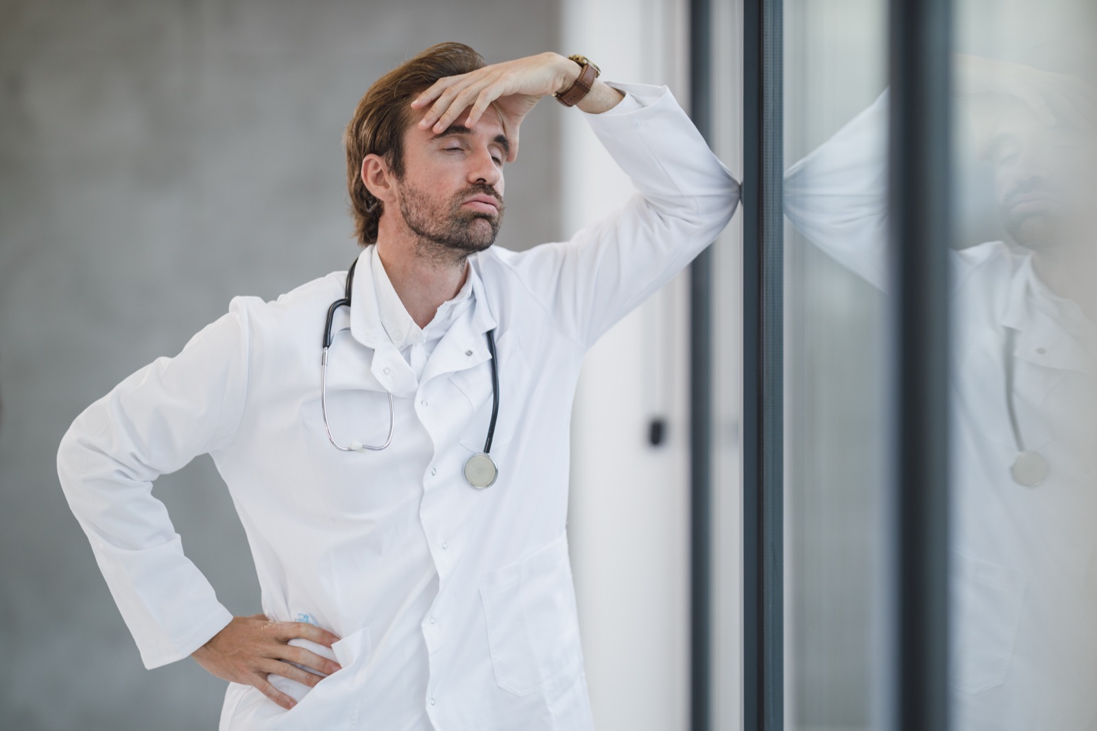 A tired doctor leaning against a clinic window
